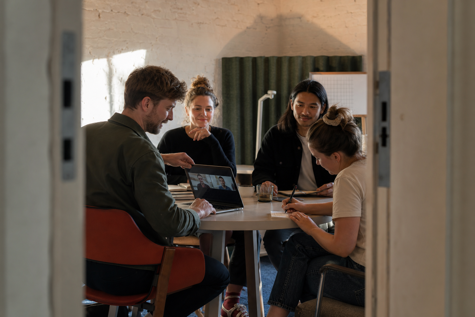 Vier collega's ronden in een kleine studio een hybride overleg af terwijl een besluit wordt genoteerd